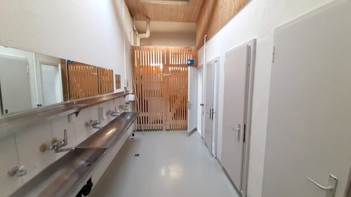 Blick in eine WC-Anlage mit einem langen Lavabo aus Chromstahl. 